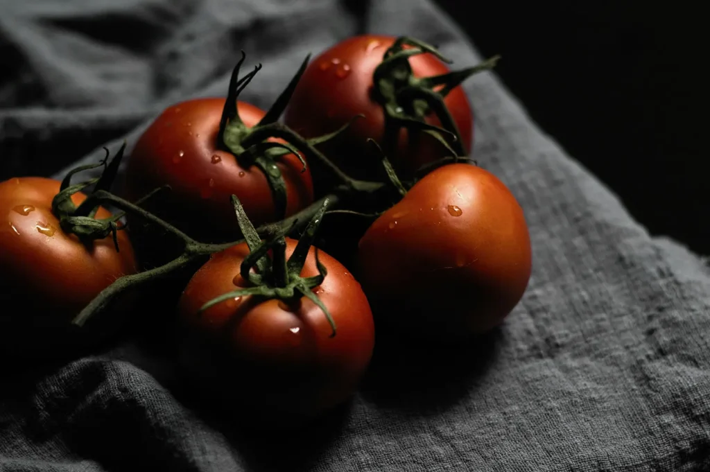 Dark moody food photography of fresh vine tomatoes on a grey rustic fabric cloth for a restaurant photography library.