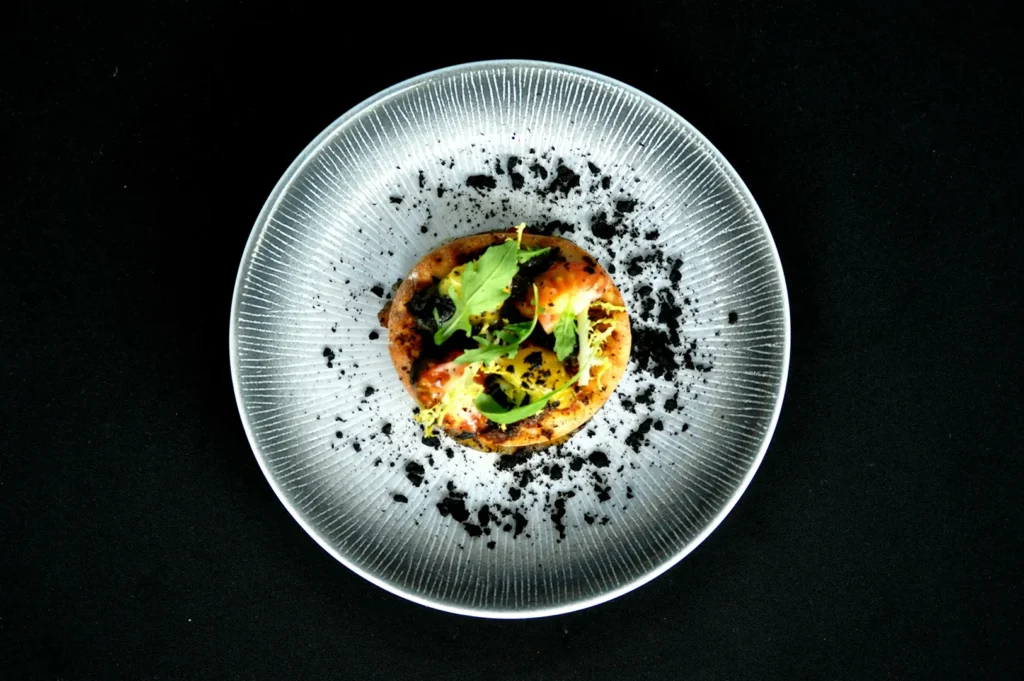 Overhead shot of a gourmet dish plated on a dark textured plate with black background for restaurant branding.