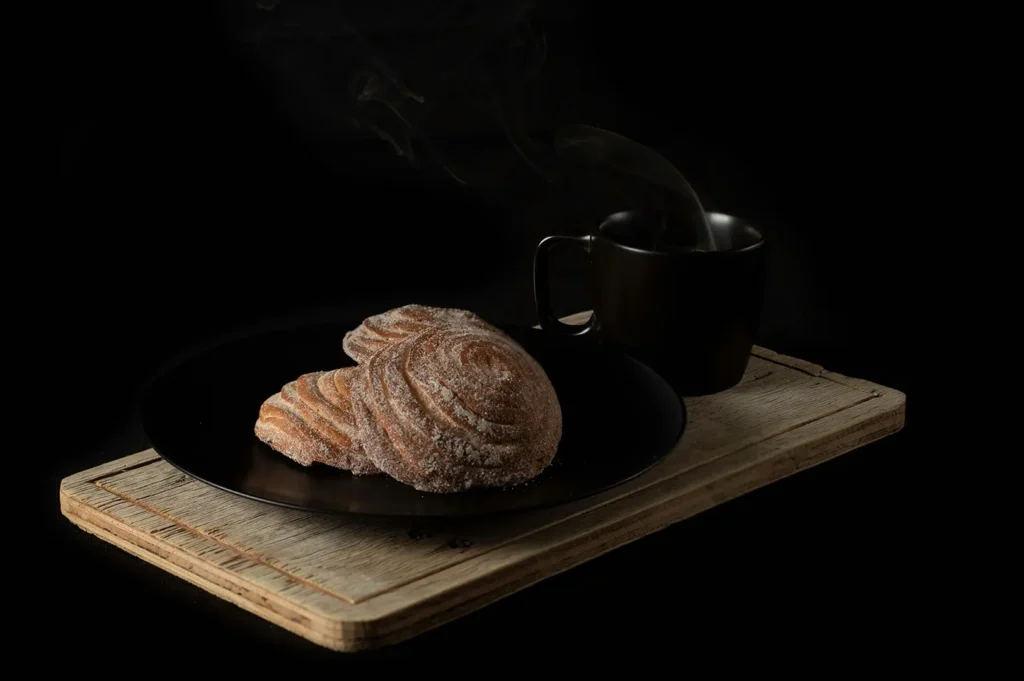 Dark moody food photography of sweet pastries and hot coffee on a wooden cutting board.