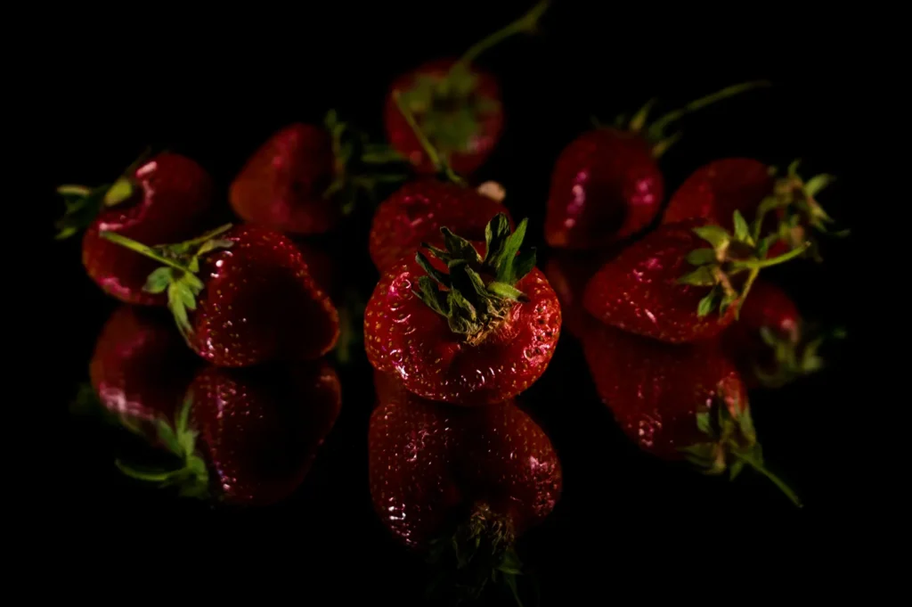 Dark moody food photography of fresh red strawberries on a black reflective surface.