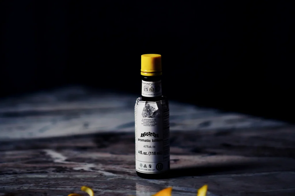 Angostura aromatic bitters bottle on a dark moody table with yellow garnish for cocktail photography.