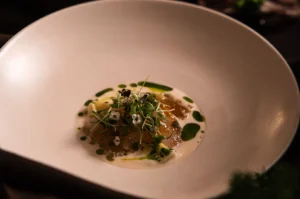 Gourmet fine dining seafood dish plated in a white bowl with herb oil photography.