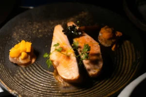 Gourmet pan-seared salmon dish with sea urchin and herbs served on a dark textured plate.