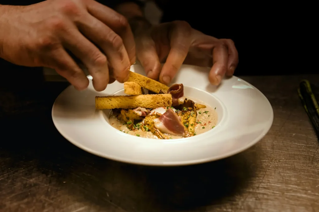 Chef plating a gourmet dish in a white bowl.