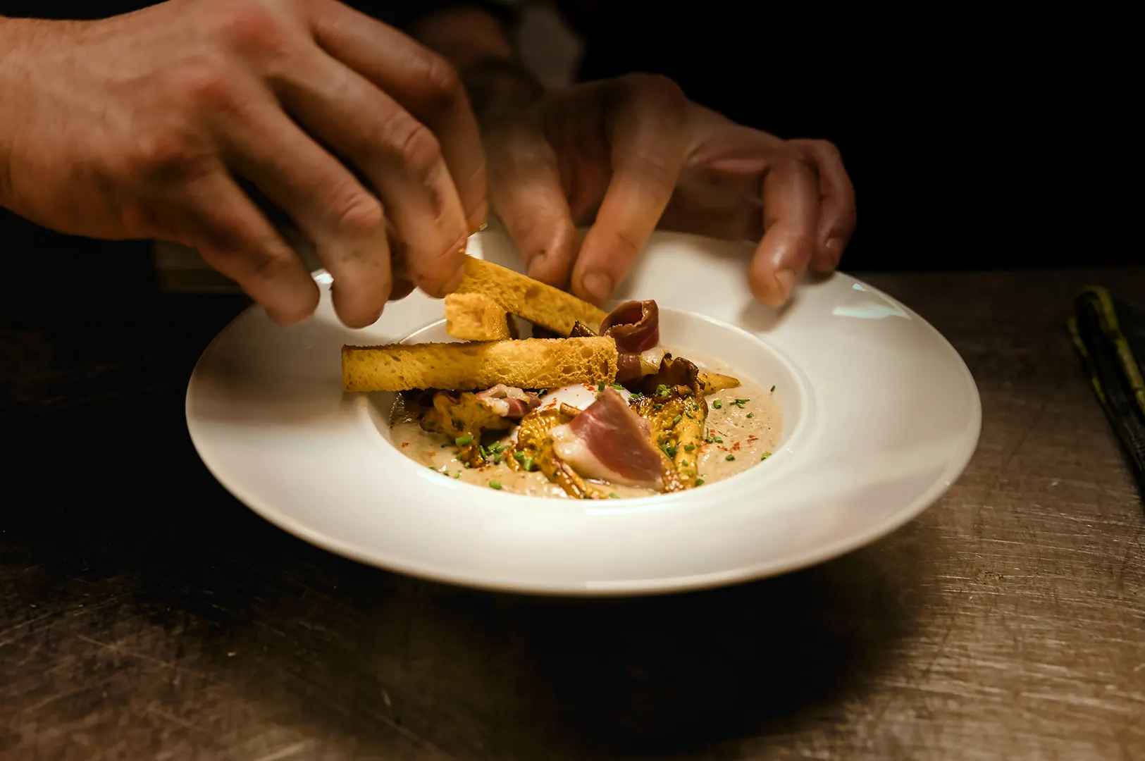 Chef plating a gourmet dish in a white bowl.