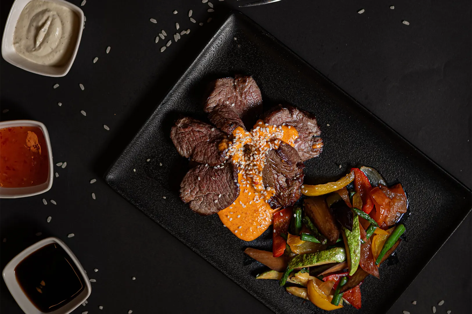 Dark moody hotel room service meal with steak and vegetables on a black plate.