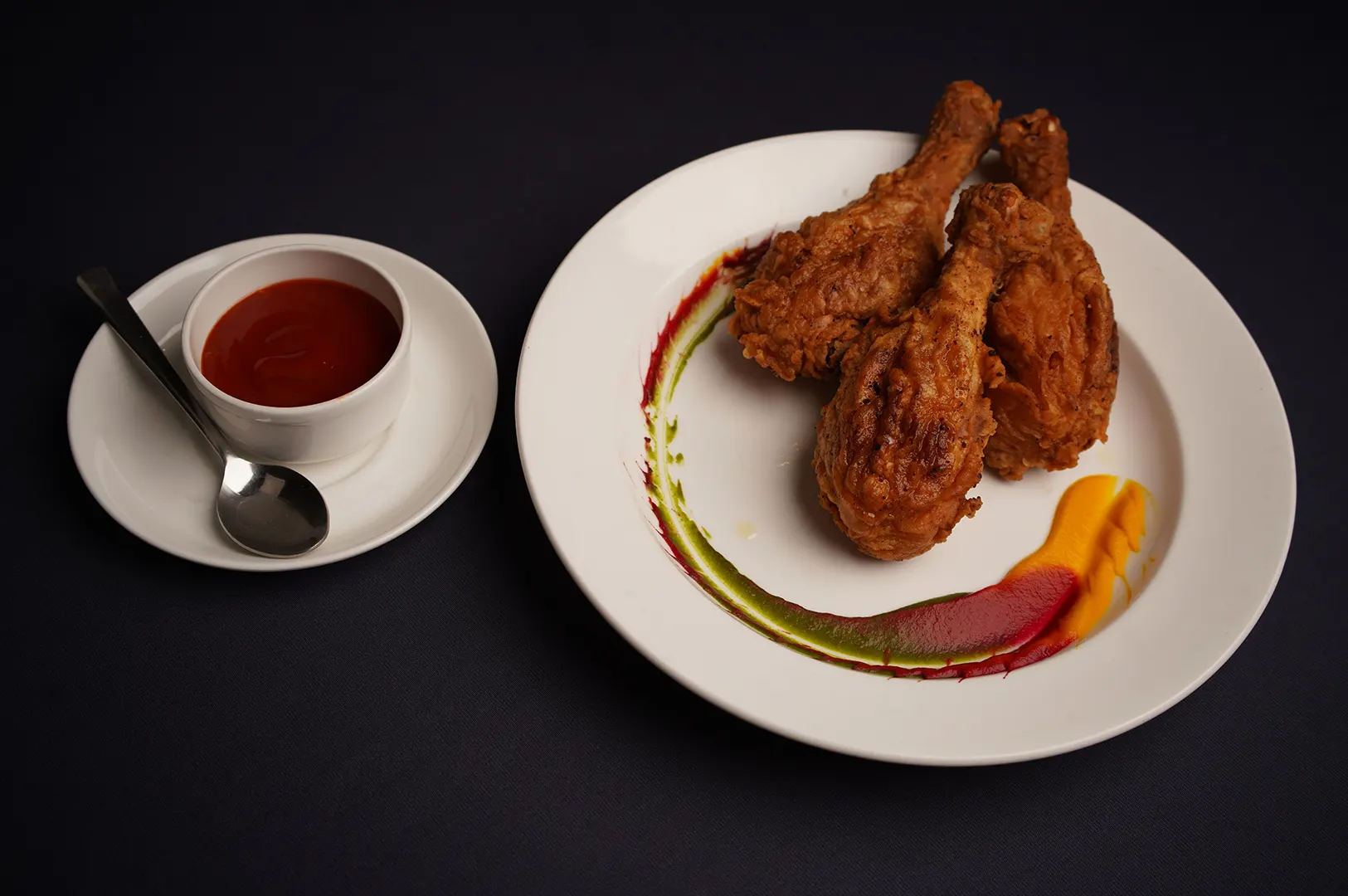 Kids menu fried chicken drumsticks on a dark plate with dipping sauce.
