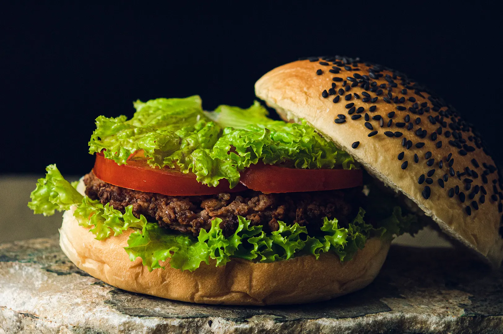 Juicy plant-based burger with fresh lettuce and tomato against a dark background.