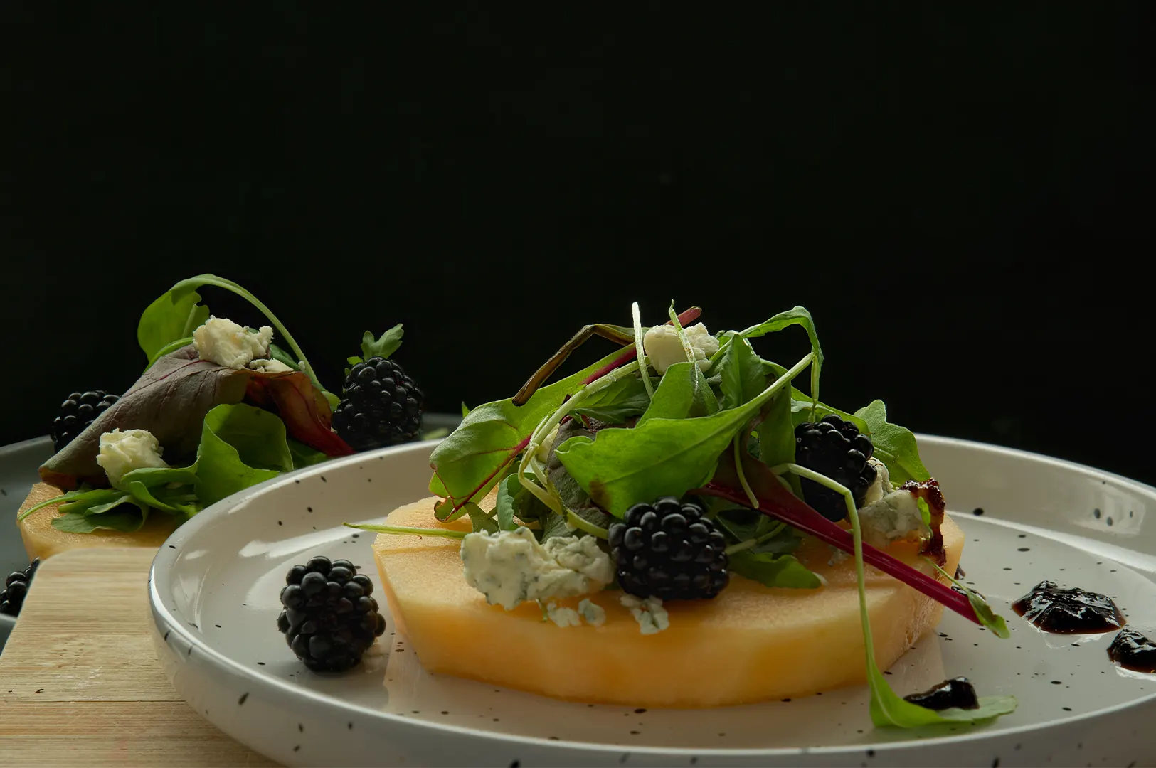 Dark and moody food photography of a gourmet salad with blackberries and cheese on a plate.