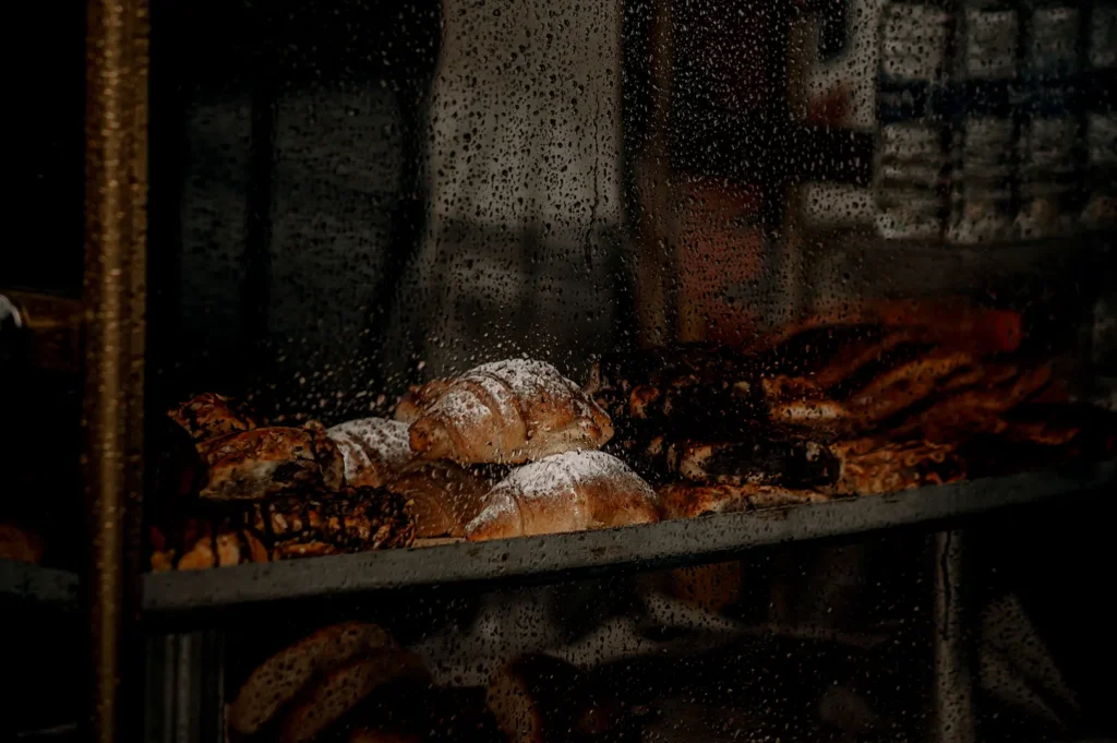 Dark moody bakery display showcasing powdered croissants and pastries inside a glass cabinet.