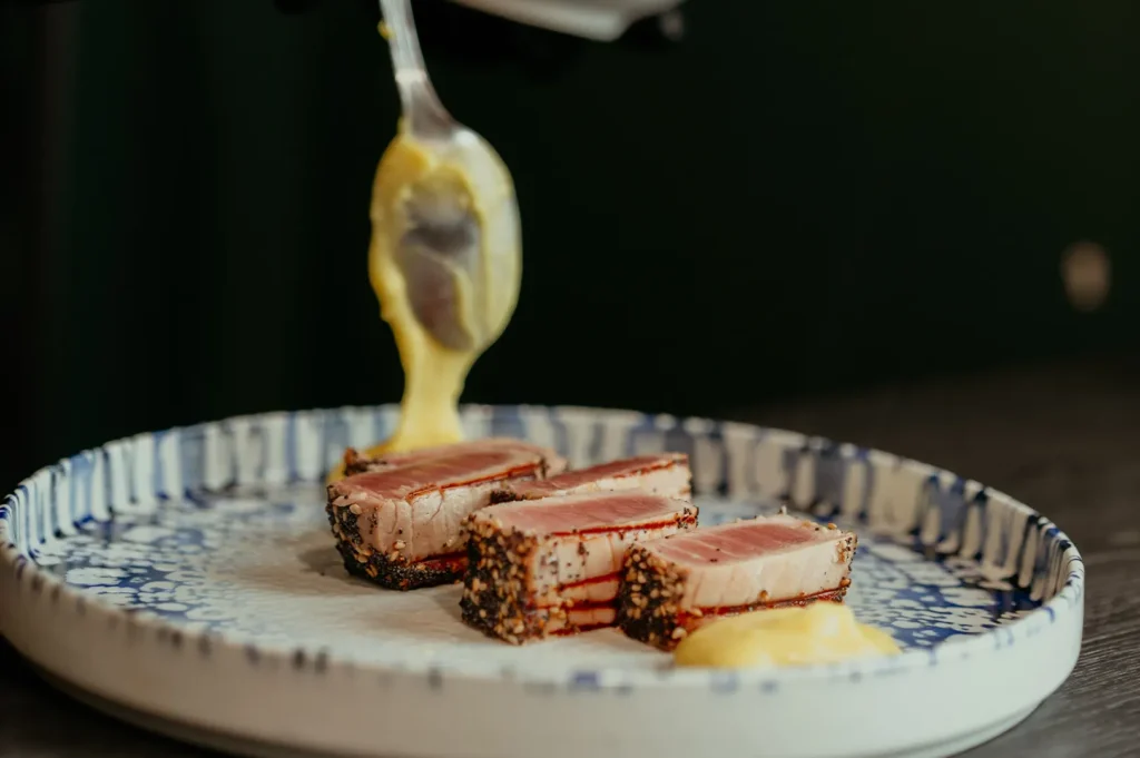 Chef adding sauce with a spoon to seared tuna plating.