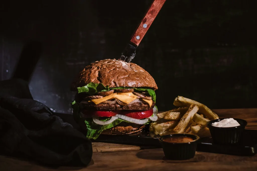 Gourmet burger with a knife, fries, and dipping sauce on a dark plate.