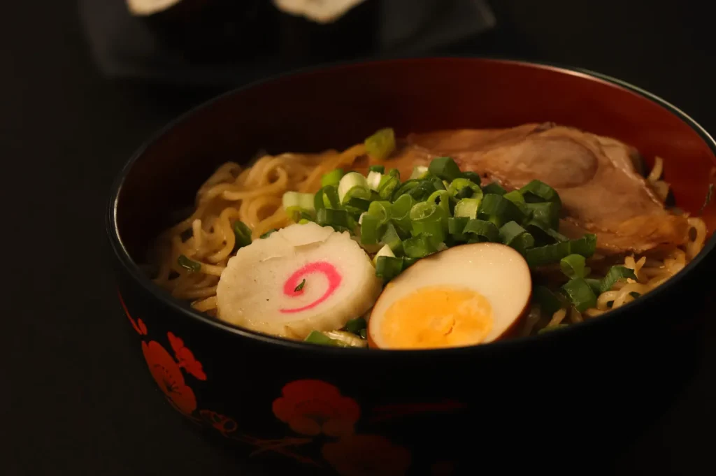 Bowl of Japanese ramen with chashu, soft-boiled egg, and narutomaki against a dark background.
