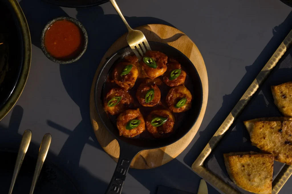 Black Pepper Sotong served in a cast iron pan with a fork, dipping sauce, and side dishes on a dark rustic table.
