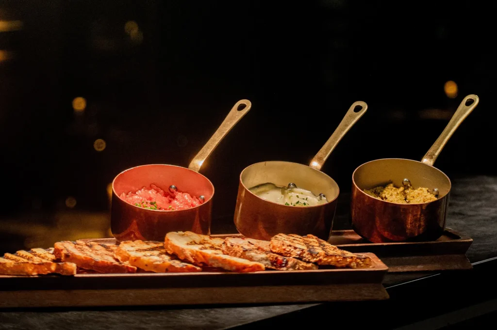 Multiple small pans with various dishes and sliced bread arranged consistently on a dark background.