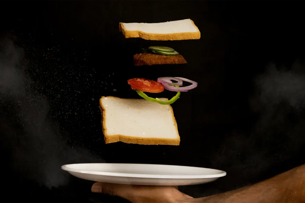 Floating sandwich ingredients with a plate against a dark background.