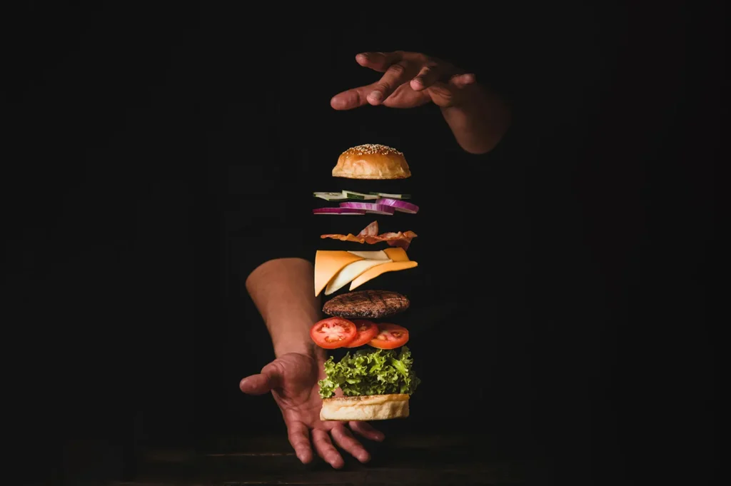 Dark food photography of a juicy plant-based burger with floating ingredients against a black background.