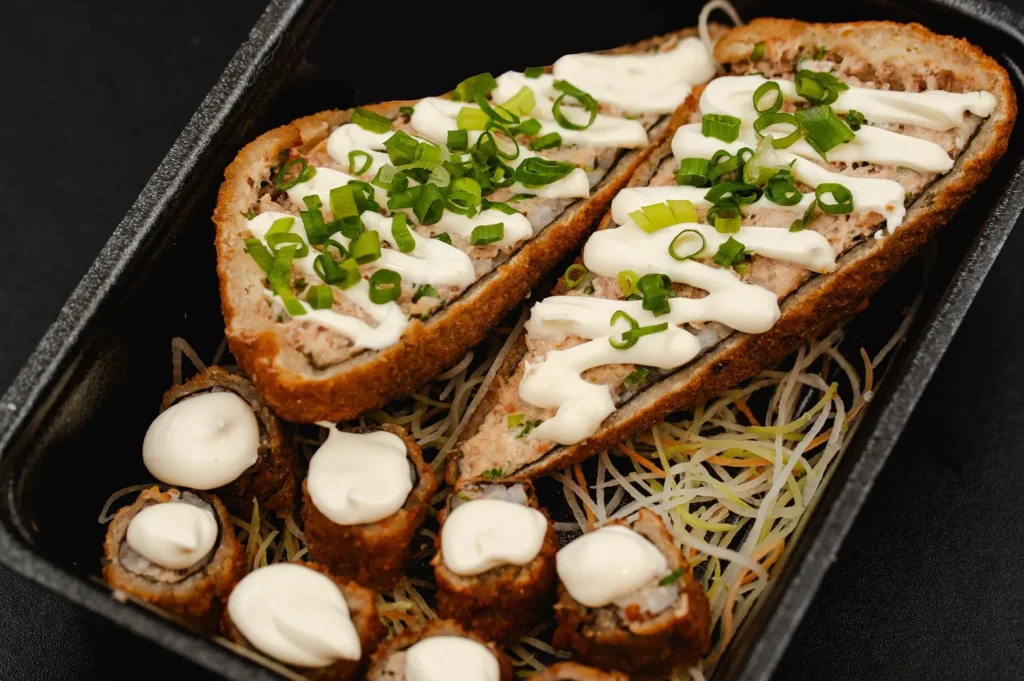 Fried sushi bento box served with mayonnaise and shredded vegetables in a black container.