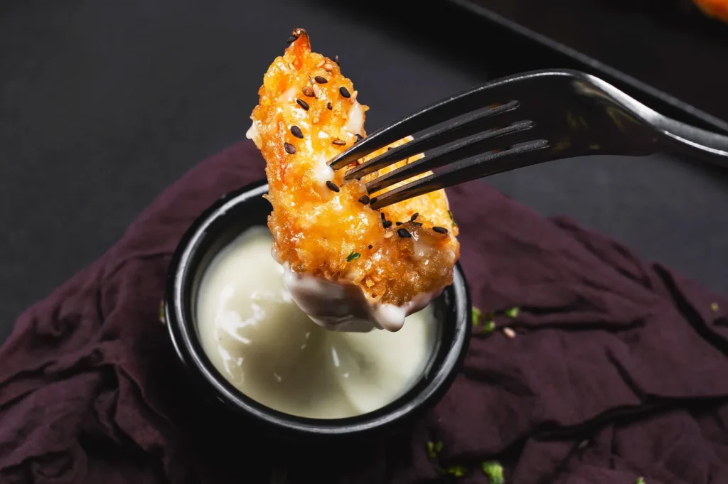 Dark moody food photography of fried food dipped in white sauce on a black background.
