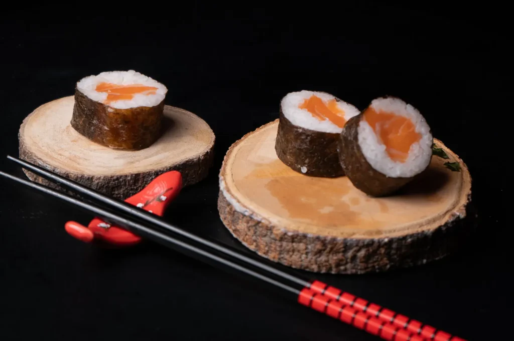 Dark and moody food photography of salmon maki sushi served on wooden slices with black background.