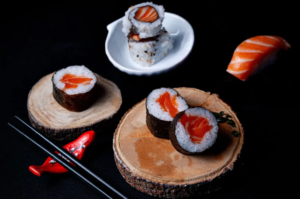 Fresh salmon sushi maki and nigiri on rustic wooden serving blocks against a black background.