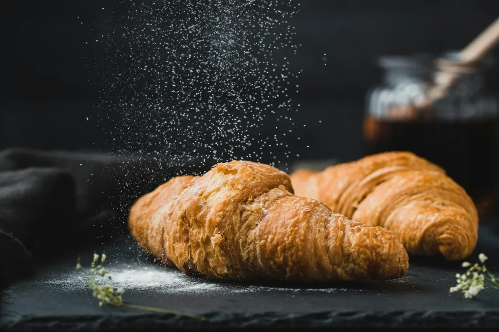 Flaky golden croissants with powdered sugar on a dark moody background.