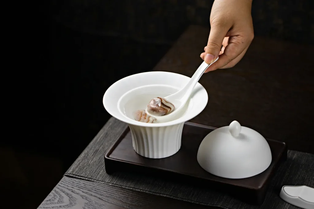 Dark moody food photography of a person using a white serving spoon to scoop a dish from a white bowl on a dark table setting.