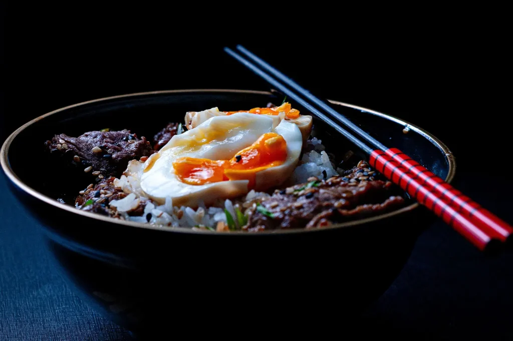 Dark moody food photography of a rice bowl topped with beef and a soft-boiled egg.
