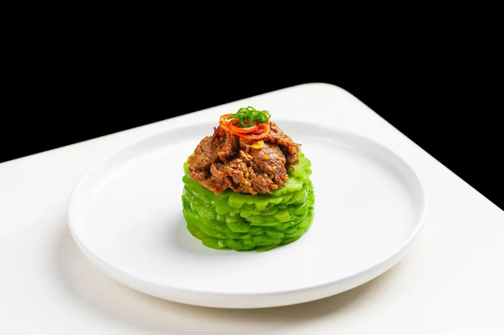 Gourmet beef dish served on sliced bitter melon on a white plate.