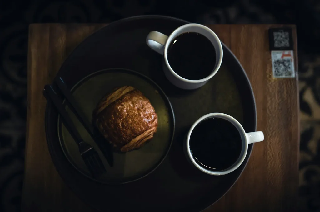 Hotel room service breakfast tray with coffee and pastry on a dark table.