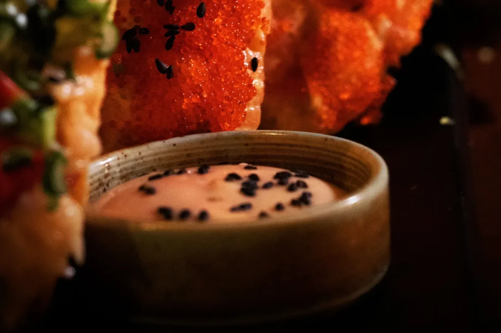 Dark moody food photography showing a sauce ramekin next to sushi rolls.