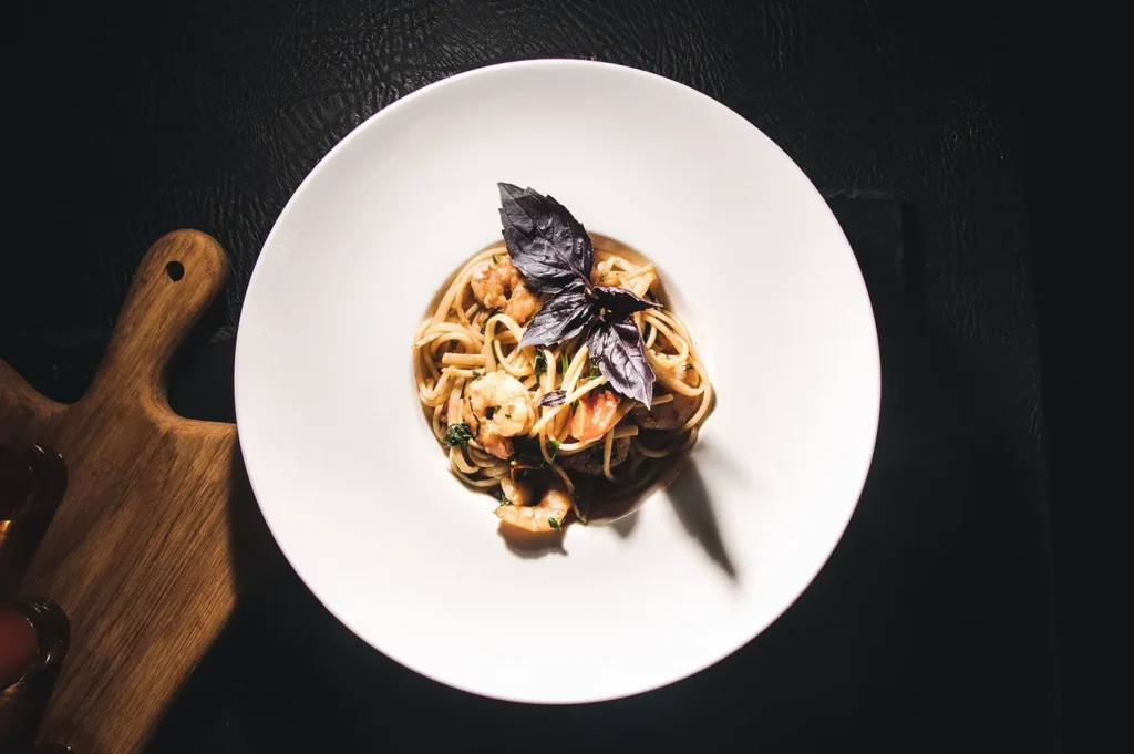 Gourmet seafood pasta hero shot plated on a white bowl with dark moody food photography styling.