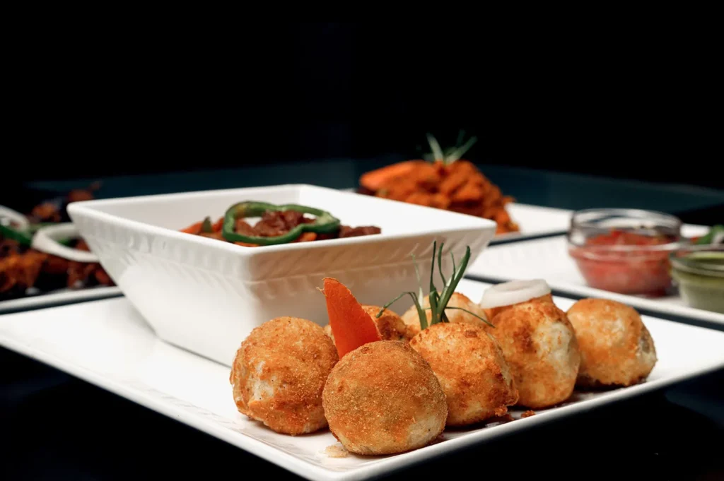 Freshly made sweet potato balls served on a white plate with a square bowl of dish against a dark background.