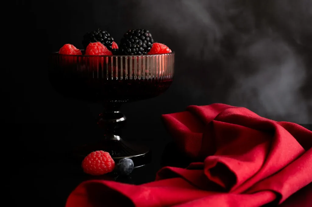 Dark moody food photography of fresh berries in a goblet with a red napkin.