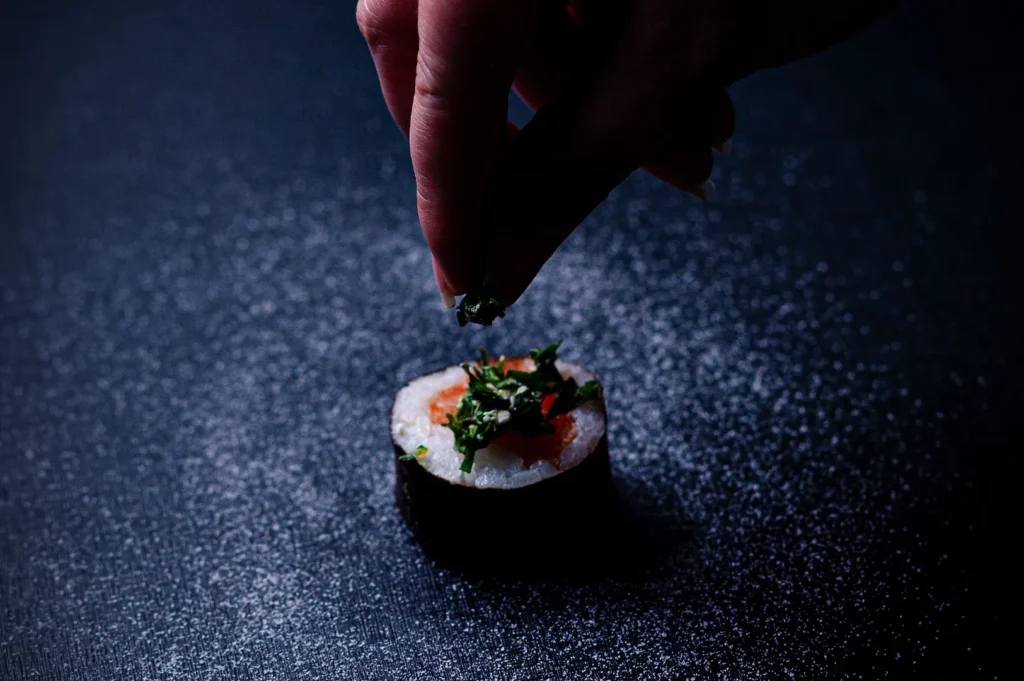 Chef garnishing sushi roll on a dark background.