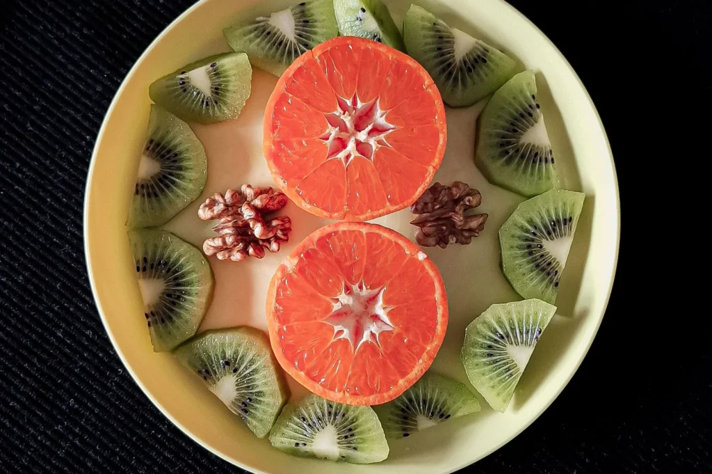 Plant-based food styling with sliced kiwi, citrus fruit, and walnuts on a plate.