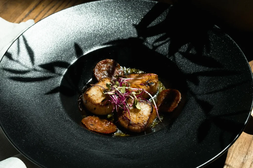 Seared sea scallops with chorizo and microgreens in a black bowl.