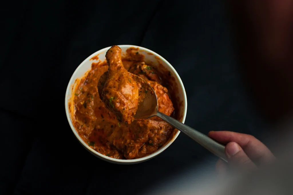Dark moody food photography of a bowl of rich curry dish being scooped with a spoon against a dark background.