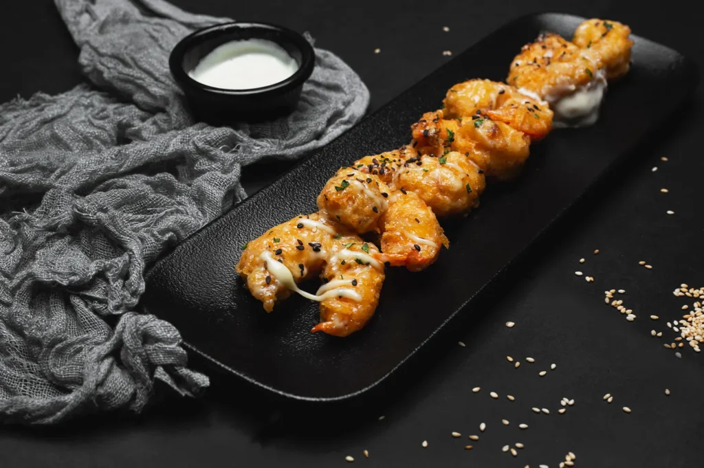 Crispy fried shrimp skewers on a dark plate with dipping sauce.