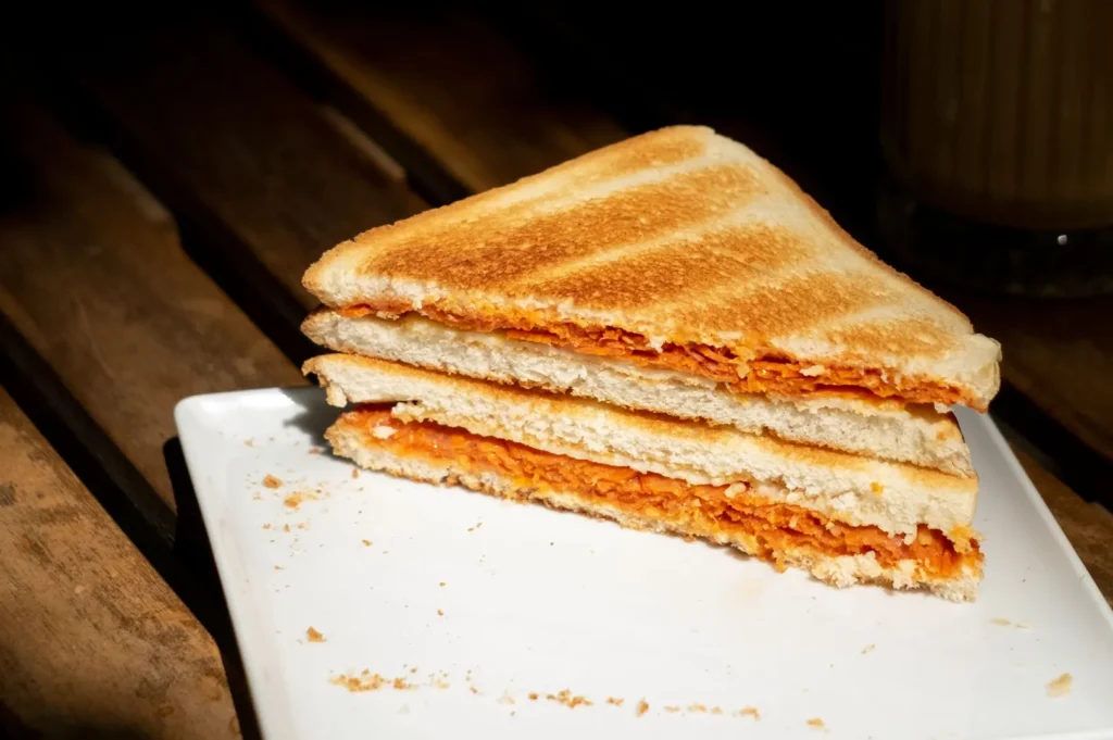 Grilled sandwich cut in half on a white plate with crumbs.
