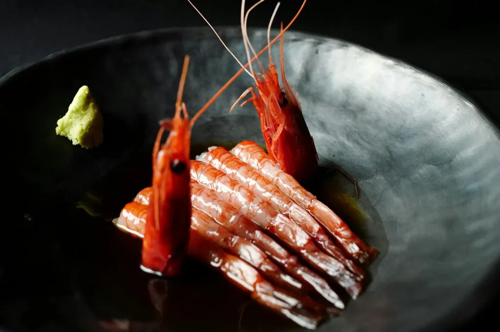 Fresh raw shrimp sashimi served on a dark plate with wasabi.