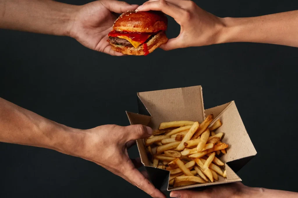 Dark and moody food photography of people sharing a gourmet burger and fries on a black background.