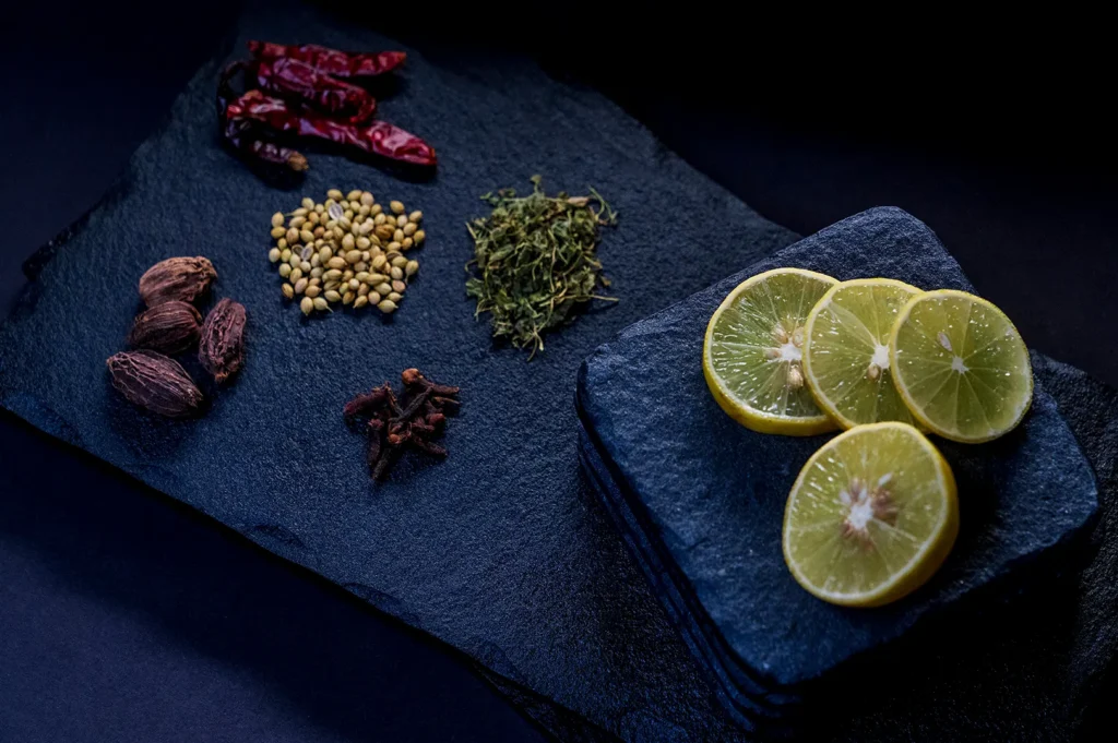 Dark and moody food photography featuring lime slices and whole spices on a black slate board.