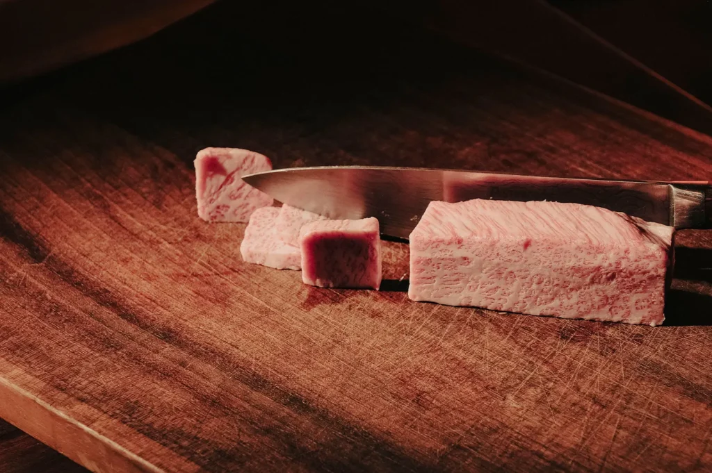 Raw Wagyu beef cubes and a knife on a cutting board.