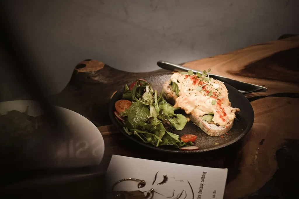 Gourmet open-faced toast with scrambled eggs and side salad on a dark plate.