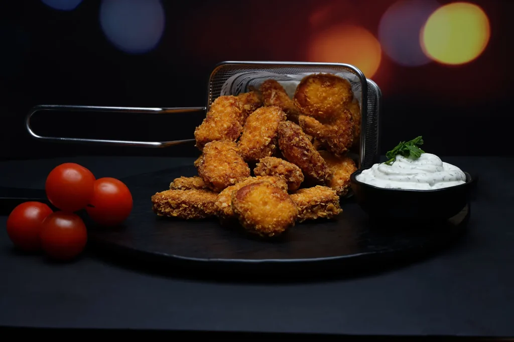 Crispy fried nuggets side dish served with dip and tomatoes in dark moody restaurant food photography.