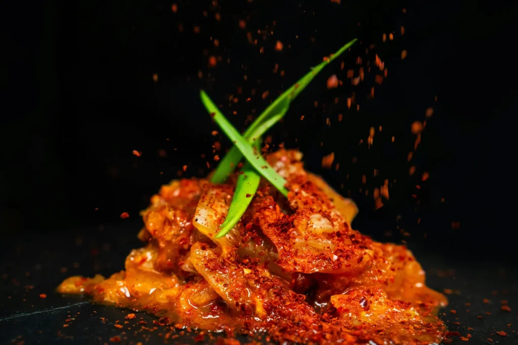 Dark and moody food photography of a spicy dish garnished with green herbs against a black background.