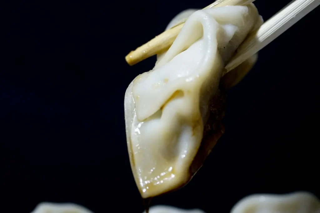 Xiao long bao held with chopsticks against a dark background.
