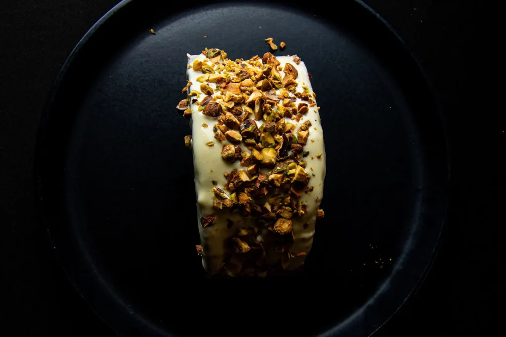Dark moody food photography of a pistachio-topped dessert on a matte black plate.